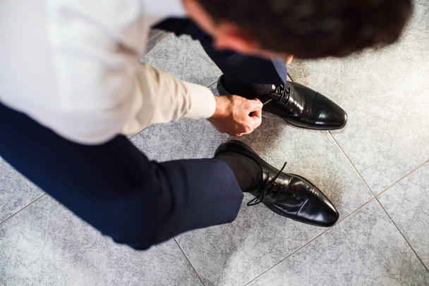 An elegant man puts on black, leather, formal shoes. Tying shoes. - Zdjęcie, obraz