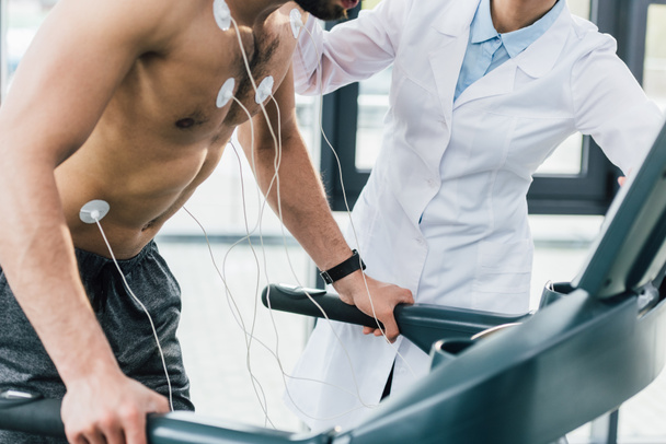 rajattu näkymä lääkäri laittaa elektrodeja paidaton urheilija kestävyystestin aikana
 - Valokuva, kuva