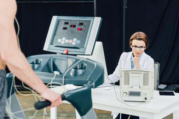 лікар за столом проводить тест на витривалість зі спортсменом у спортзалі
 - Фото, зображення