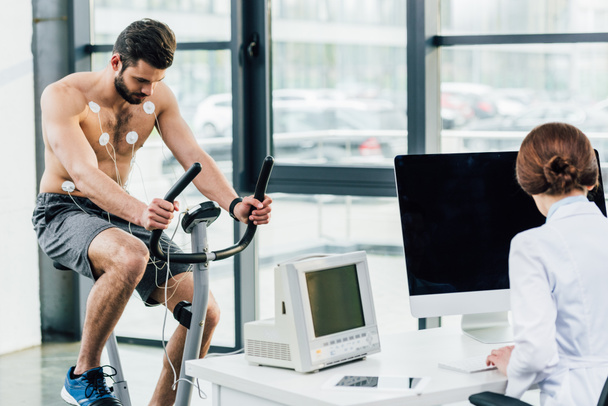 γιατρός διεξάγει δοκιμή αντοχής με αθλητή με ηλεκτρόδια στο γυμναστήριο - Φωτογραφία, εικόνα