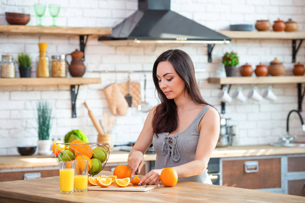 sporty young woman is cutting fresh orange for fruit juice in the kitchen. Horizontal indoors shot - Foto, Imagem