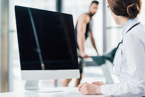selective focus of doctor sitting near computer with blank screen in gym - Fotoğraf, Görsel