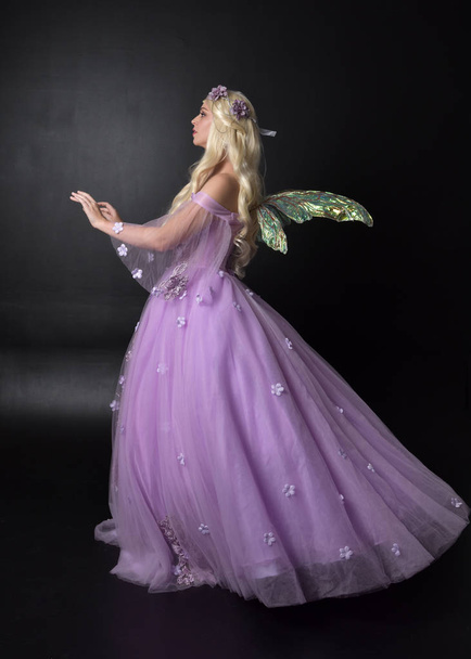Pełna długość Portret blond dziewczyna ubrana w fantazyjne bajki inspirowane kostium, długa fioletowa suknia balowa z bajki skrzydła, stojący stwarzają na ciemnym tle Studio. - Zdjęcie, obraz