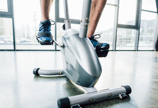 cropped view of sportsman training on elliptical machine at gym - Foto, imagen
