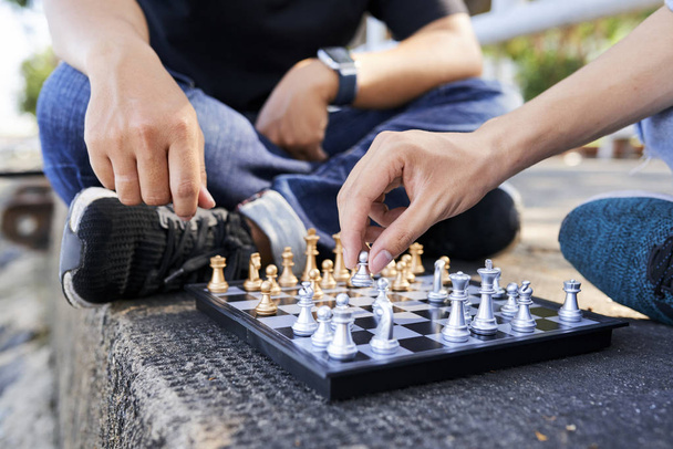 Крупный план мужчин, сидящих на земле с шахматной доской и играющих вместе в шахматы
 - Фото, изображение