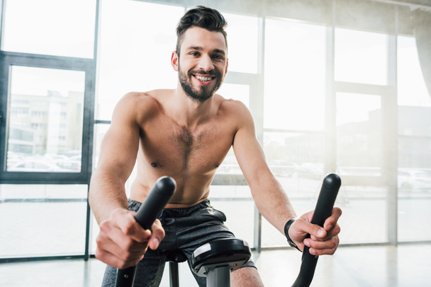smiling handsome sportsman training on elliptical machine at gym - Foto, immagini