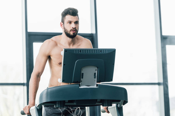 без рубашки красивый спортсмен с электродами работает на беговой дорожке во время испытаний на выносливость в тренажерном зале
 - Фото, изображение