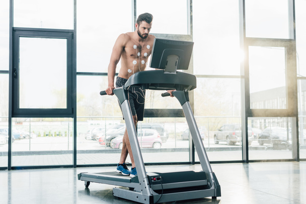 beau sportif torse nu avec des électrodes fonctionnant sur tapis roulant pendant l'essai d'endurance dans la salle de gym
 - Photo, image