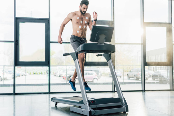 handsome sportsman with electrodes running on treadmill during endurance test in gym - Foto, imagen