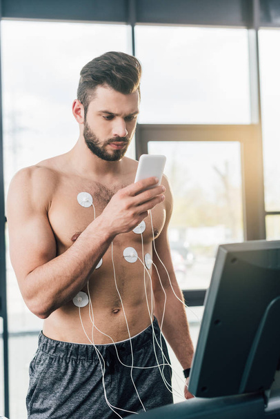 sportsman with smartphone running on treadmill during endurance test in gym - Фото, зображення