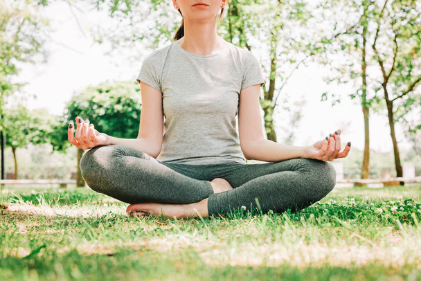 Mujer joven en pose de loto sentada sobre hierba verde en el parque. Concepto de calma y meditación
. - Foto, Imagen