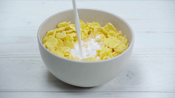 Milch in knusprigen und leckeren Cornflakes in Schüssel auf Holztisch gießen  - Filmmaterial, Video