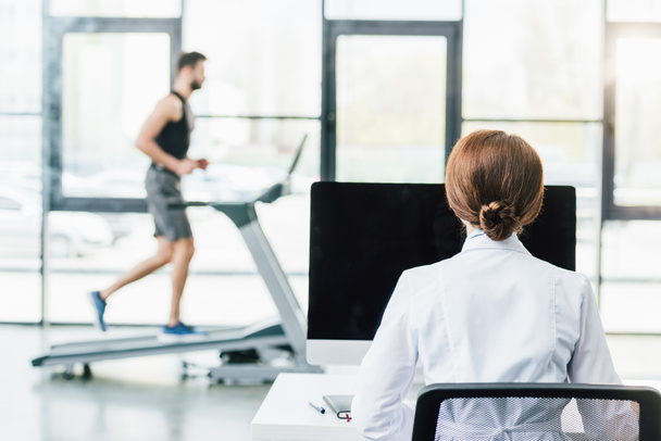 doctor using computer while sportsman running on treadmill during endurance test in gym - Foto, Imagen