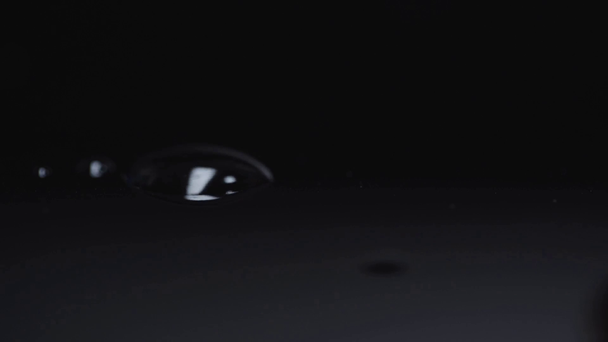 selektiver Fokus von Regentropfen, die auf eine kleine Pfütze auf schwarz fallen  - Filmmaterial, Video