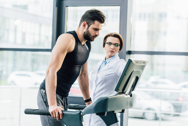 sportsman training on treadmill near doctor during endurance test in gym - Fotografie, Obrázek