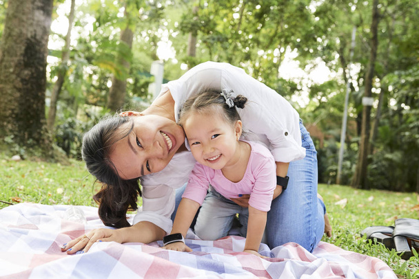 glückliche junge Asiatin und ihre lächelnde Tochter spielen an einem Sommertag im Park - Foto, Bild