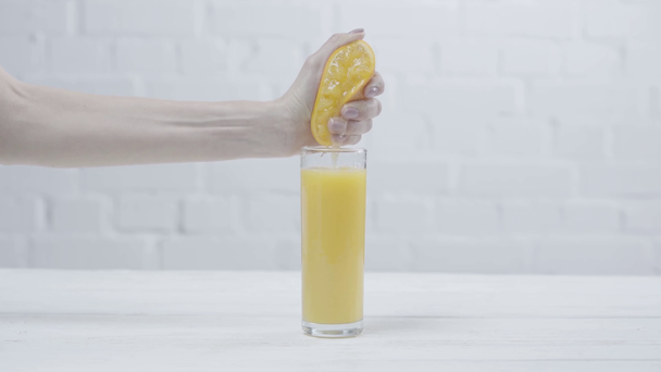 vista recortada de la mujer exprimiendo naranja cerca del vaso de jugo de naranja
  - Imágenes, Vídeo