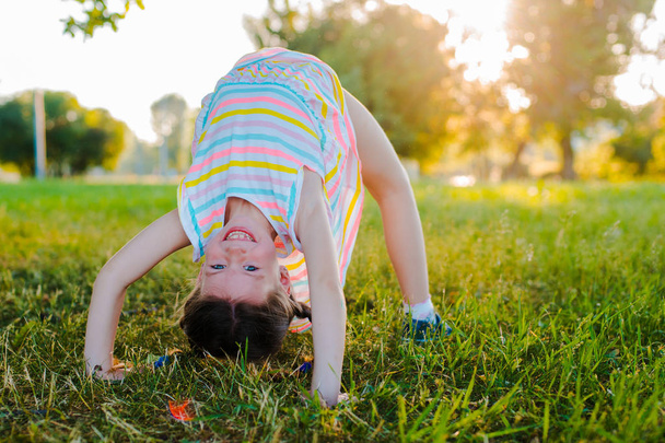 Happy baby standing upside down on green grass in summer Park. - 写真・画像