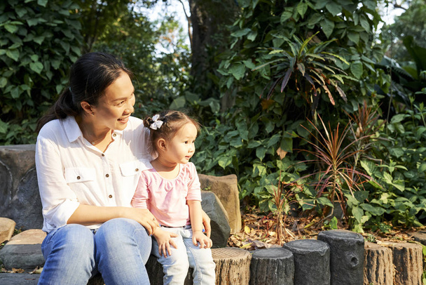 Happy young Asian woman and her daughter resting on wooden stump - Fotoğraf, Görsel