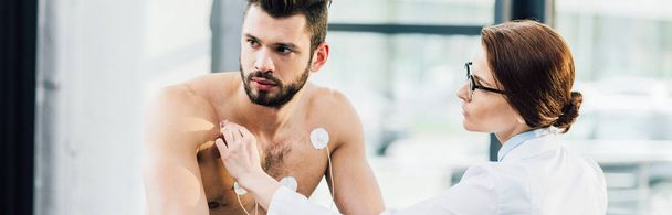 plan panoramique du médecin mettant des électrodes sur l'homme torse nu pendant le test d'endurance
 - Photo, image