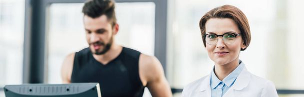 sportsman running on treadmill near doctor looking at camera during endurance test in gym - Фото, зображення