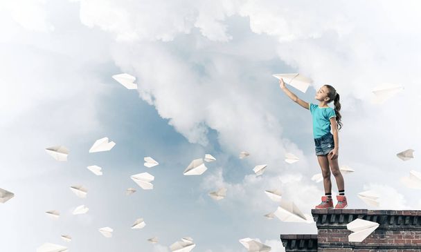 Cute happy kid girl on building top playing with paper plane - Foto, imagen