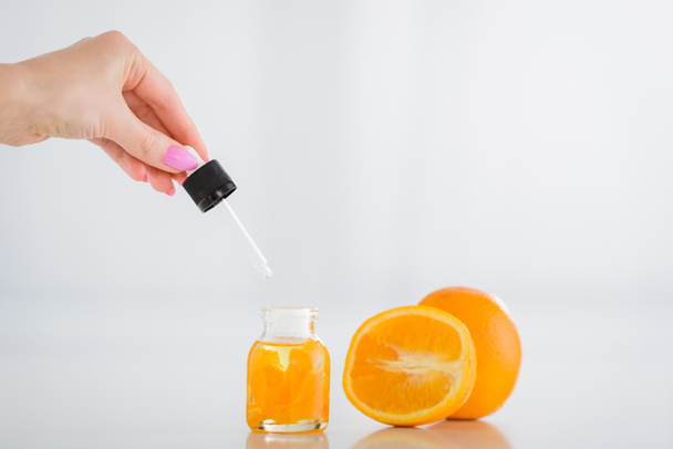 vista recortada de la mujer sosteniendo cayó cerca de botella con aceite esencial de naranja y naranjas frescas sobre fondo blanco
 - Foto, Imagen