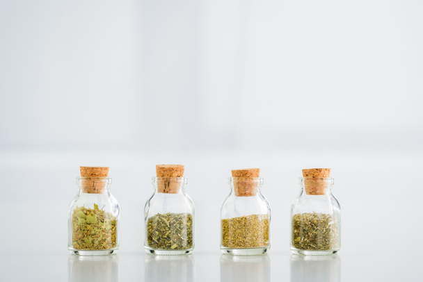 corked jars with dried herbs on white background with copy space - Fotó, kép