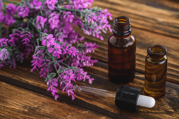 bottles with essential oils, dropper  and heather flowers on wooden surface - Foto, afbeelding