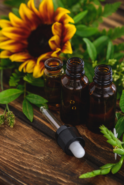bottles with essential oils, dropper and sunflower on wooden surface - Photo, Image