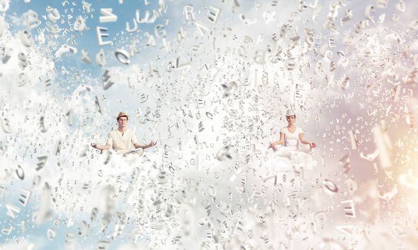 Молодая пара закрывает глаза и смотрит сосредоточенно во время медитации между летящими буквами в воздухе с облачным пейзажем на заднем плане
. - Фото, изображение