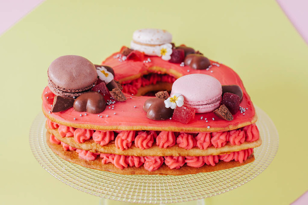 A pink cake. Decoration from sweets, macaroons, hocolate. Sweet present.  - Foto, Bild