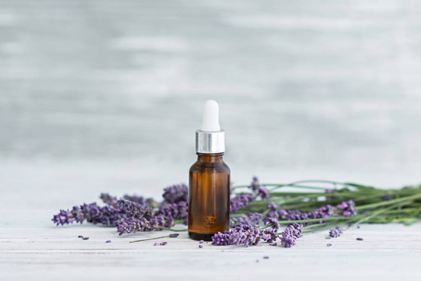 Lavender herbal oil and lavender flowers on grey wooden background. - Foto, imagen