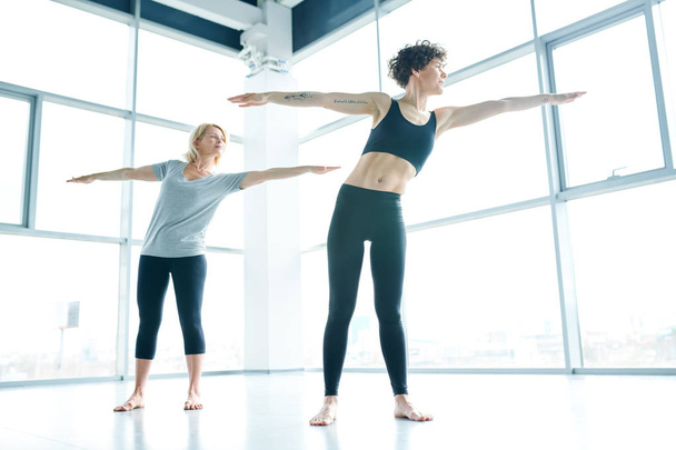 jovem ajuste ativo mulher e seu maduro grupo no sportswear estendendo seus braços enquanto exercitando no ginásio
 - Foto, Imagem
