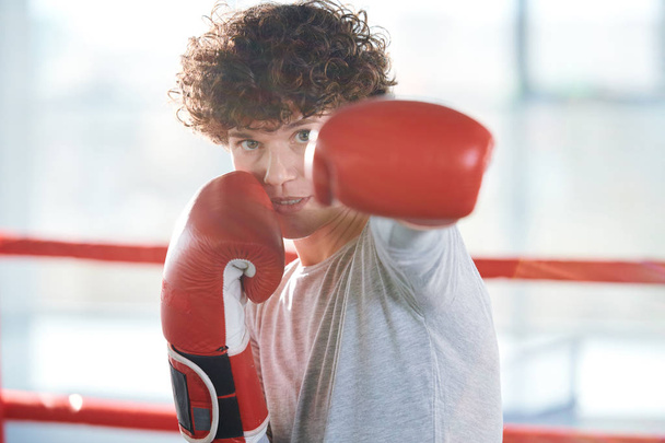 Активная молодая женщина смотрит на тебя во время боя в боксёрских перчатках во время тренировки перед соревнованиями
 - Фото, изображение
