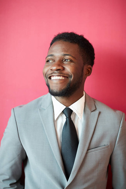 Young cheerful African-american businesman with toothy smile and beard standing in isolation on pink background - Foto, afbeelding