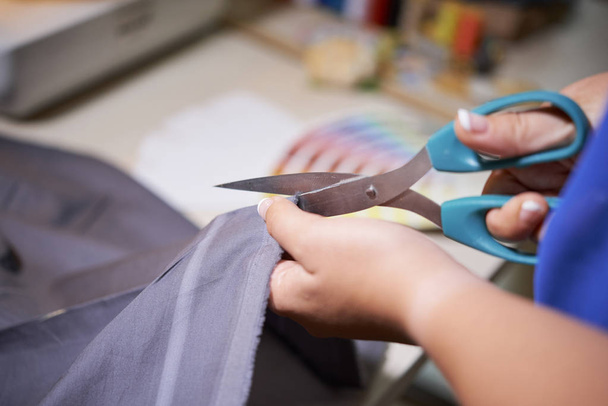 Close-up van naaister met behulp van een schaar om stof te snijden voor toekomstig kostuum in atelier - Foto, afbeelding