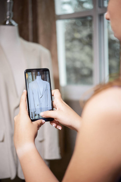 Close-up of young designer photographing new jacket on mannequin on her mobile phone for her collection - Fotoğraf, Görsel
