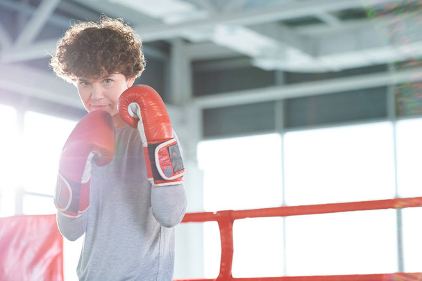 Ένα νεαρό κορίτσι με αυτοπεποίθηση σε ρούχα γυμναστικής και κόκκινα γάντια πυγμαχίας να σε κοιτάζει ενώ θα πολεμάς - Φωτογραφία, εικόνα