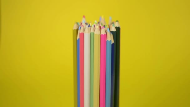 Gekleurde potloden die met elkaar verbonden zijn vallen ongeordend op gele achtergrond, eenheid en samenwerking van organisatie concept. - Video