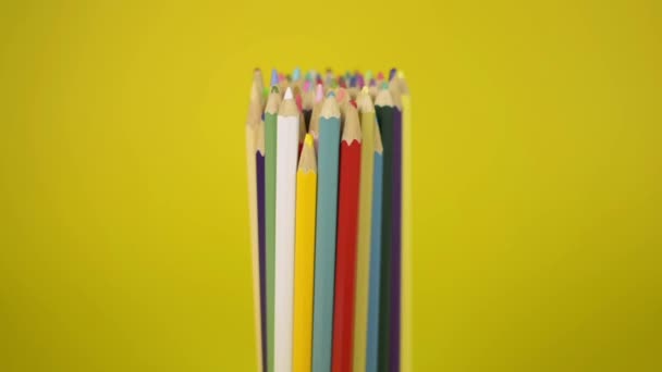 Gekleurde potloden die met elkaar verbonden zijn vallen ongeordend op gele achtergrond, eenheid en samenwerking van organisatie concept. - Video