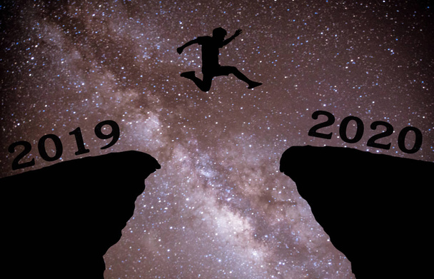 A young man jump between 2019 and 2020 years over night sky with stars and through on the gap of hill  silhouette evening colorful sky. happy new year 2020 - Foto, Imagem