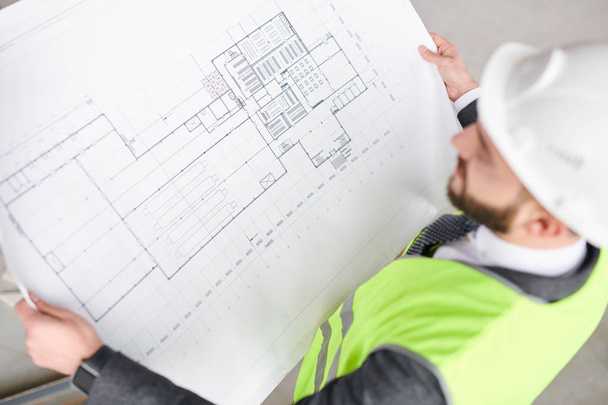 Contemporary engineer looking at construction sketch on blueprint in his hands while working over new project - Zdjęcie, obraz