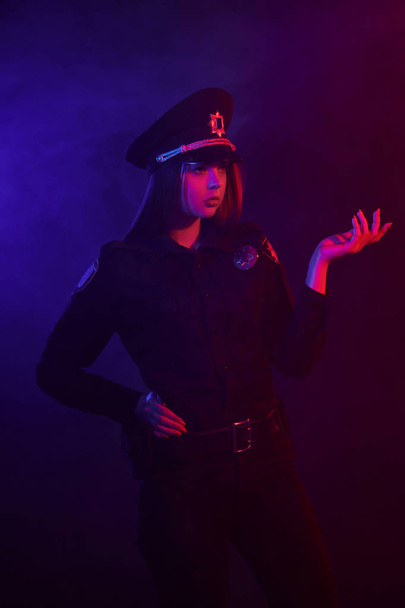 Mujer policía pelirroja posando para la cámara sobre un fondo negro con retroiluminación roja y azul
. - Foto, Imagen