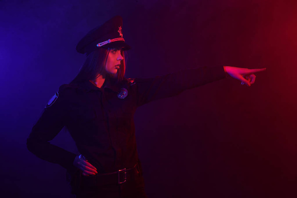 赤毛の女性警察官は、赤と青のバックライトと黒の背景に対してカメラのためにポーズをとっています. - 写真・画像