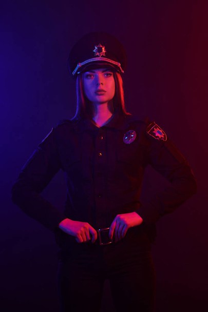 Une policière rousse pose pour la caméra sur un fond noir avec un rétroéclairage rouge et bleu
. - Photo, image