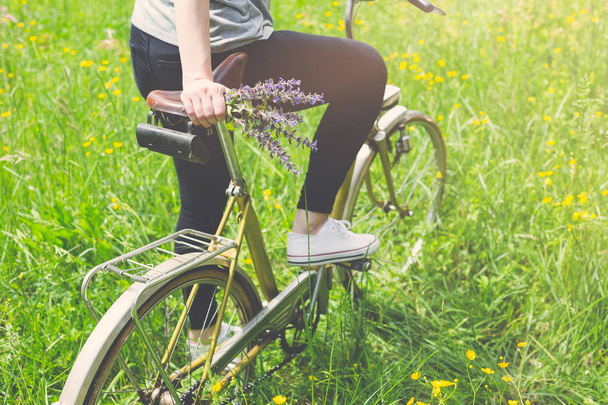Nahaufnahme einer Frau auf einem Oldtimer-Fahrrad in der Natur. Sommer- oder Frühjahrskonzept. - Foto, Bild