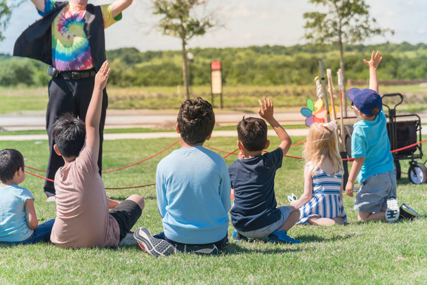 Vue arrière enfants multiculturels sur herbe prairie levant les mains dans le jeu de plein air
 - Photo, image