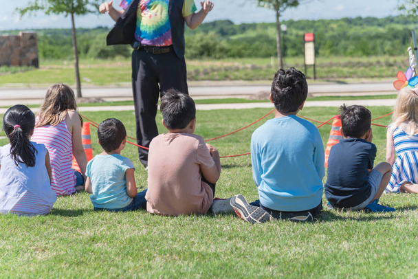 Πίσω θέα πολυπολιτισμικά παιδιά σε γρασίδι λιβάδι ακούγοντας προπονητή του εξωτερικού παιχνιδιού - Φωτογραφία, εικόνα