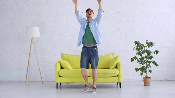 fröhlicher junger Mann tanzt im geräumigen Wohnzimmer und blickt in die Kamera - Filmmaterial, Video